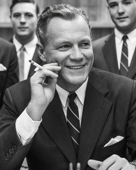 Walter Pell at his desk, smiling, holding a cigarette